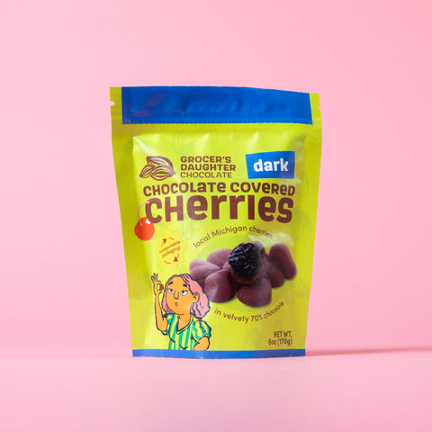 Packaging of Grocery's Daughter Dark Chocolate Covered Cherries on a pink background