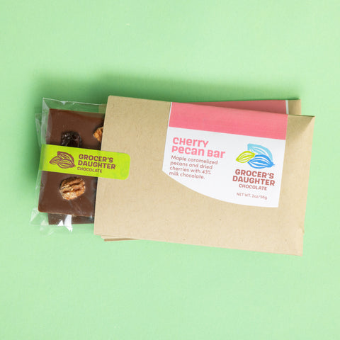 A packaged chocolate bar product with visible pieces of cherry and nuts, and labels indicating 'Cherry Pecan' flavor and organic ingredients.